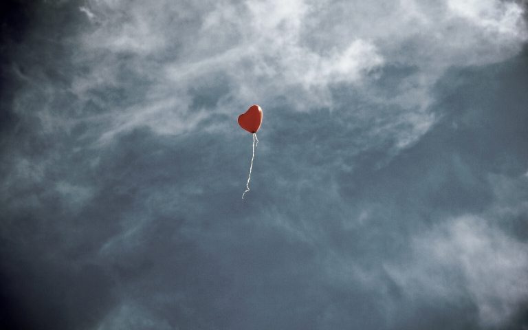 Ein herzförmiger, roter Ballon flieg in den Himmel. Alles ist in sehr gedeckten Farben gehalten